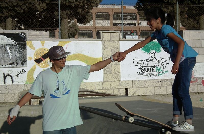 A. Szostek uczy jazdy na deskorolce dziewczynkę w Palestynie.